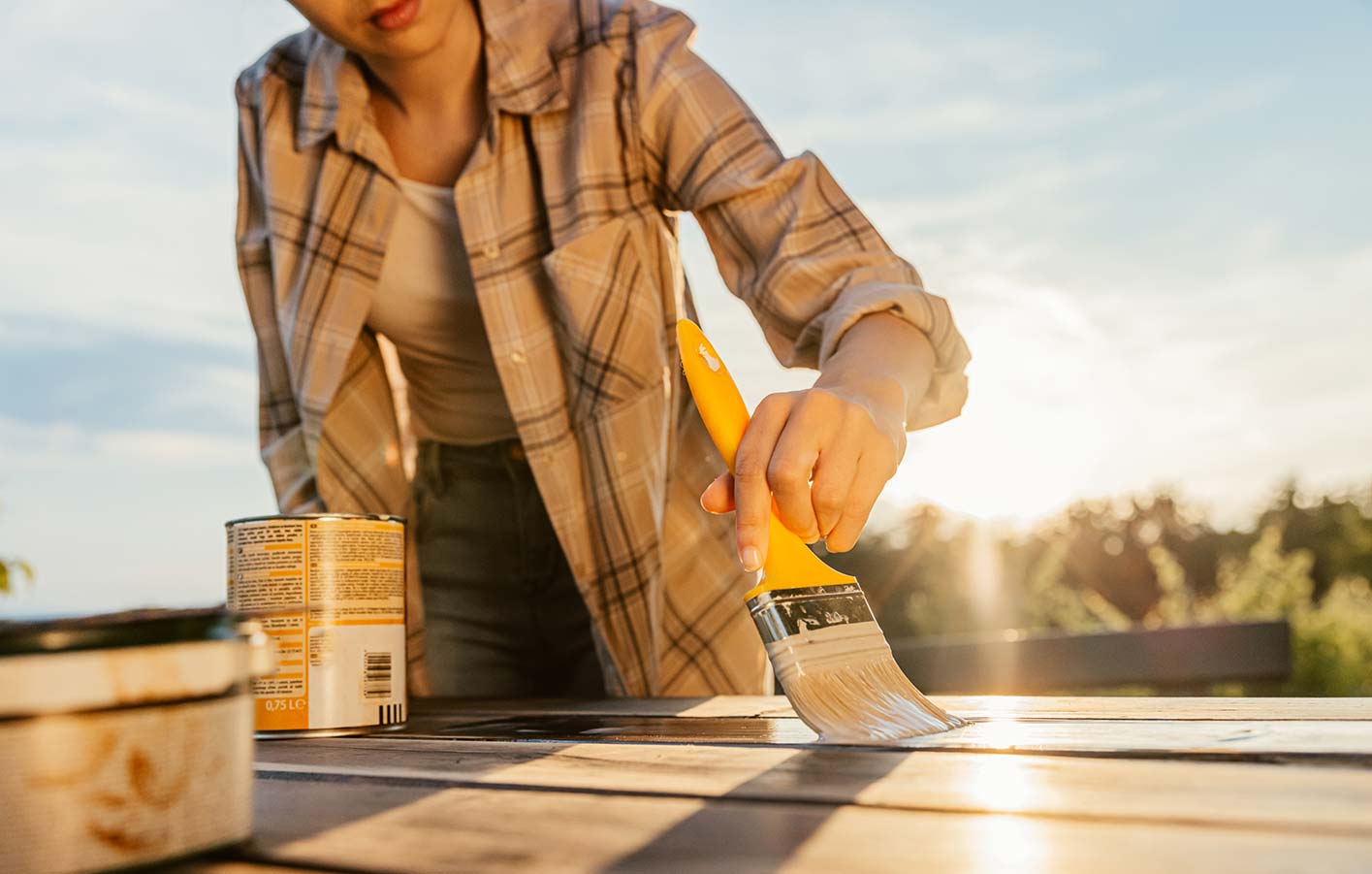 Frau streicht einen Gartentisch in der Sonne